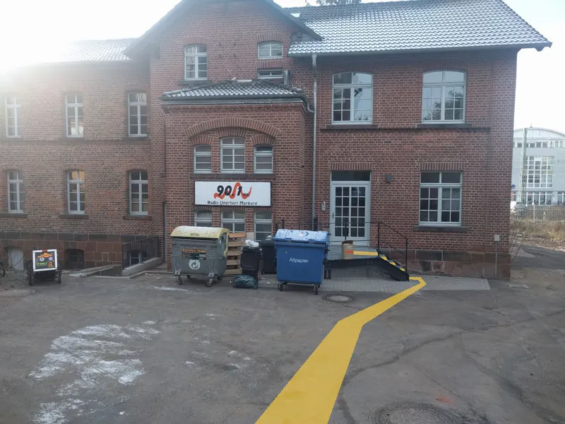Das Backsteingebäude des Funkhauses mit dem Schild „Radio Unerhört Marburg“; ein gelber Streifen führt zur Eingangstür rechts.